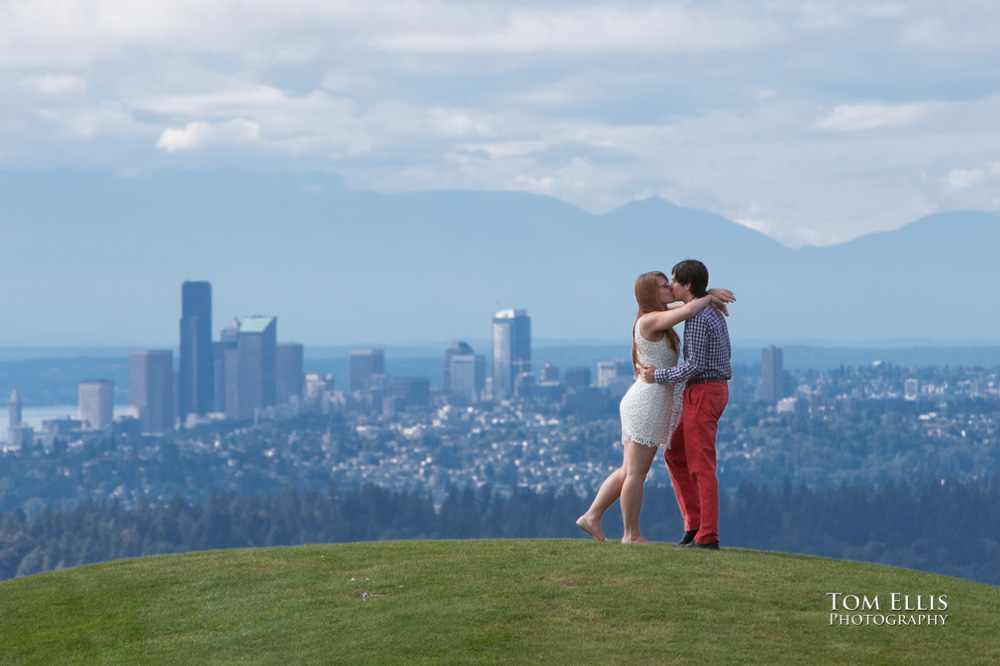 Engagement photo of couple standing and kissing on hilltop with city of Seattle in the background, at Newcastle Golf Club