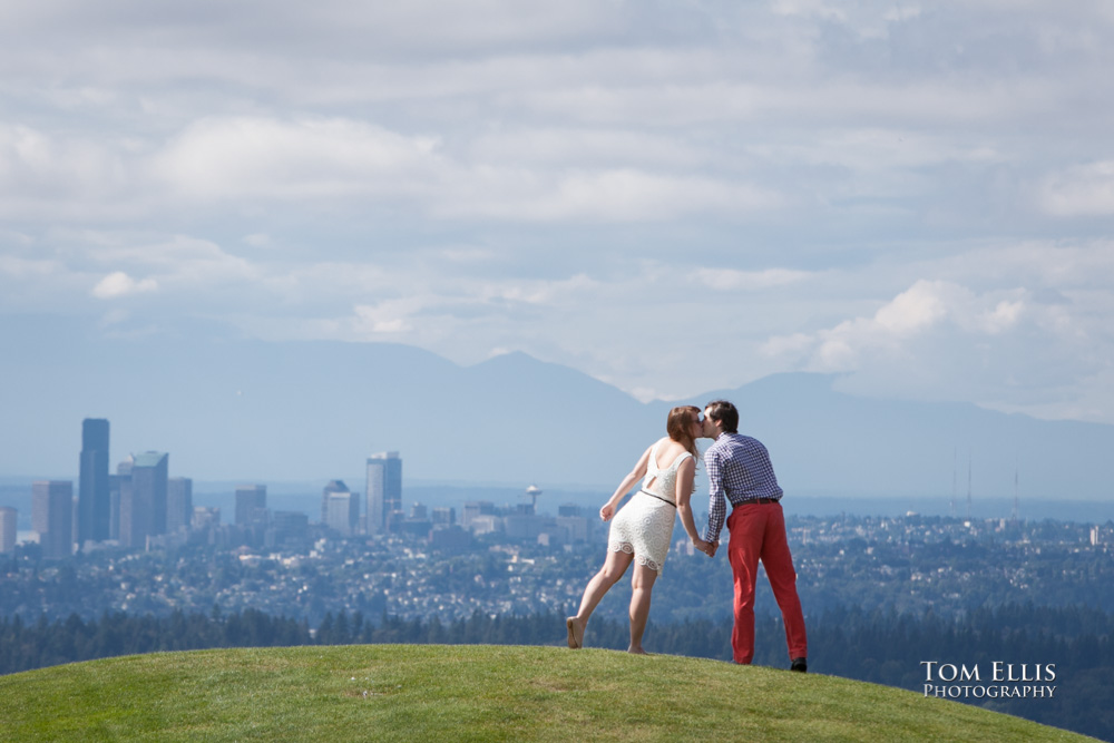 Engagement photo of couple kissing while standing on hilltop with city of Seattle in the background, at Newcastle Golf Club