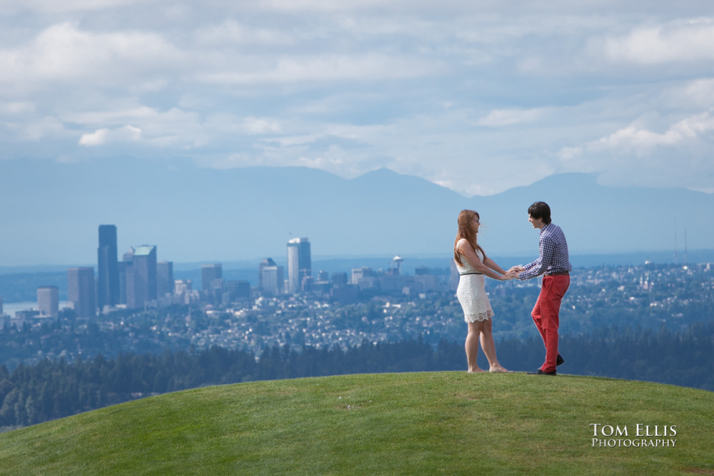 Engagement photo of couple standing on hilltop with city of Seattle in the background, at Newcastle Golf Club