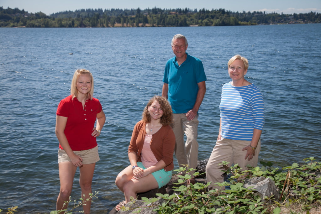 Family photo of couple with their two grown daughters, posed on the waterfront along Lake Washington