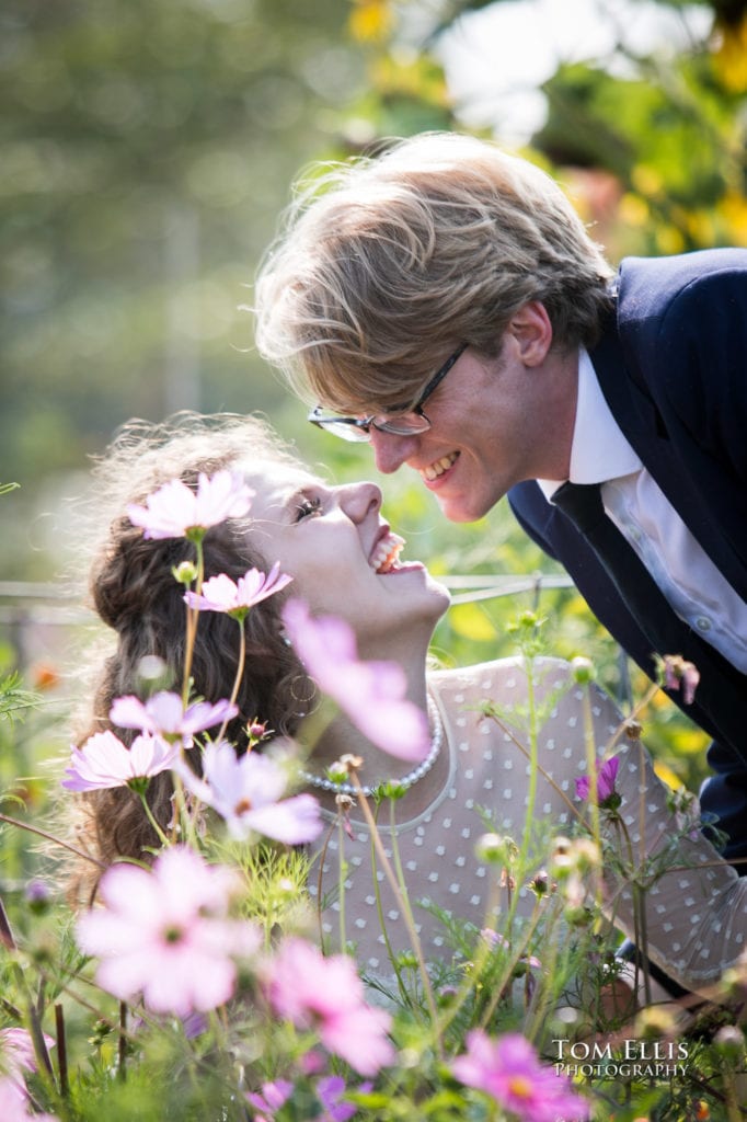 Romantic close up photo of bride and groom in a field of beautiful flowers, as the laughing bride looks up at the groom