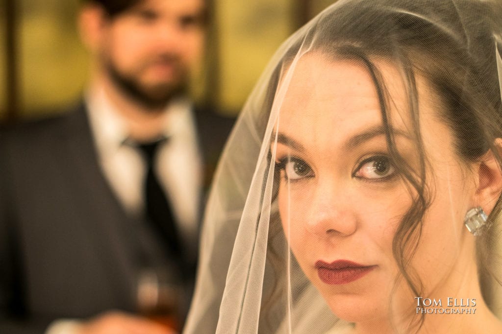 Close up photo of bride in veil, with groom in the background