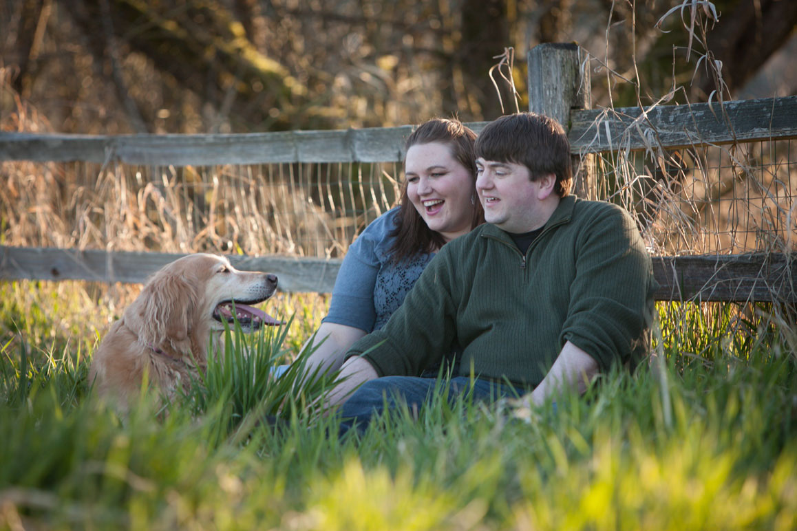 Engagement photo of couple with their Golden Retriever, sitting in the grass at Marymoor Park