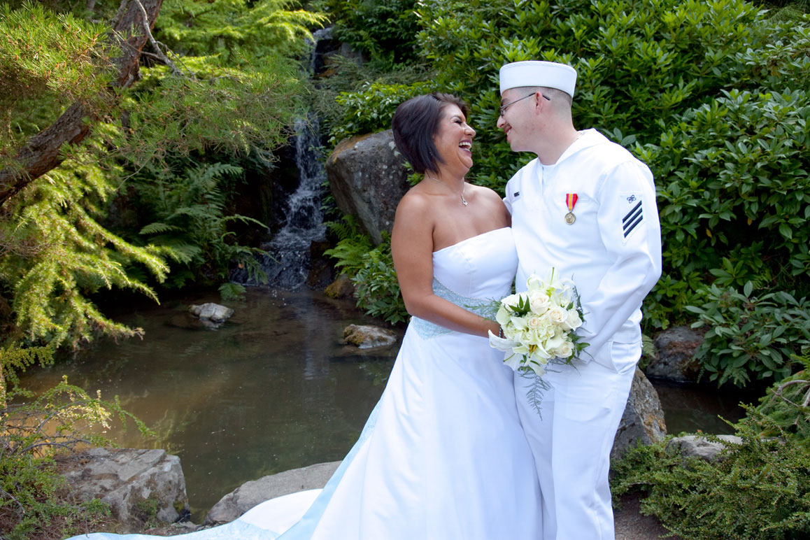Bride with groom in Navy uniform hugging next to waterfall at Kubota Gardens