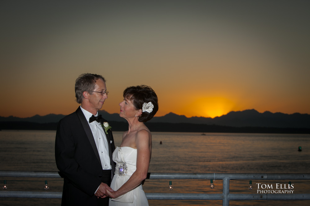 Bride and groom photographed against a background of the sun setting behind the Olympic Mountains during their Seattle area wedding at Ray's Boathouse