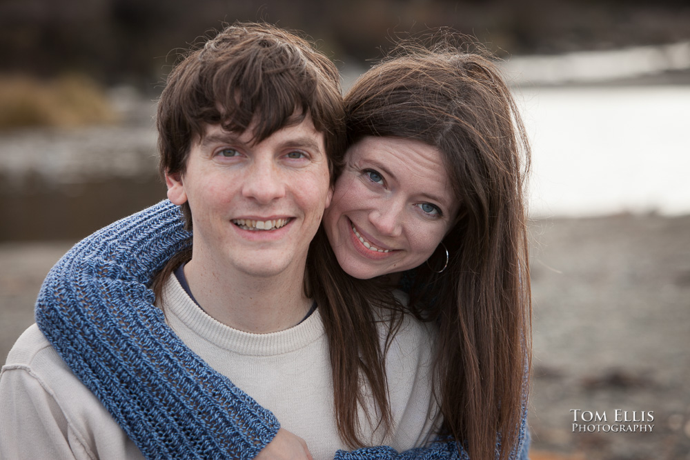 Close up engagement photo, woman behind man with her arm draped around his shoulder and chest