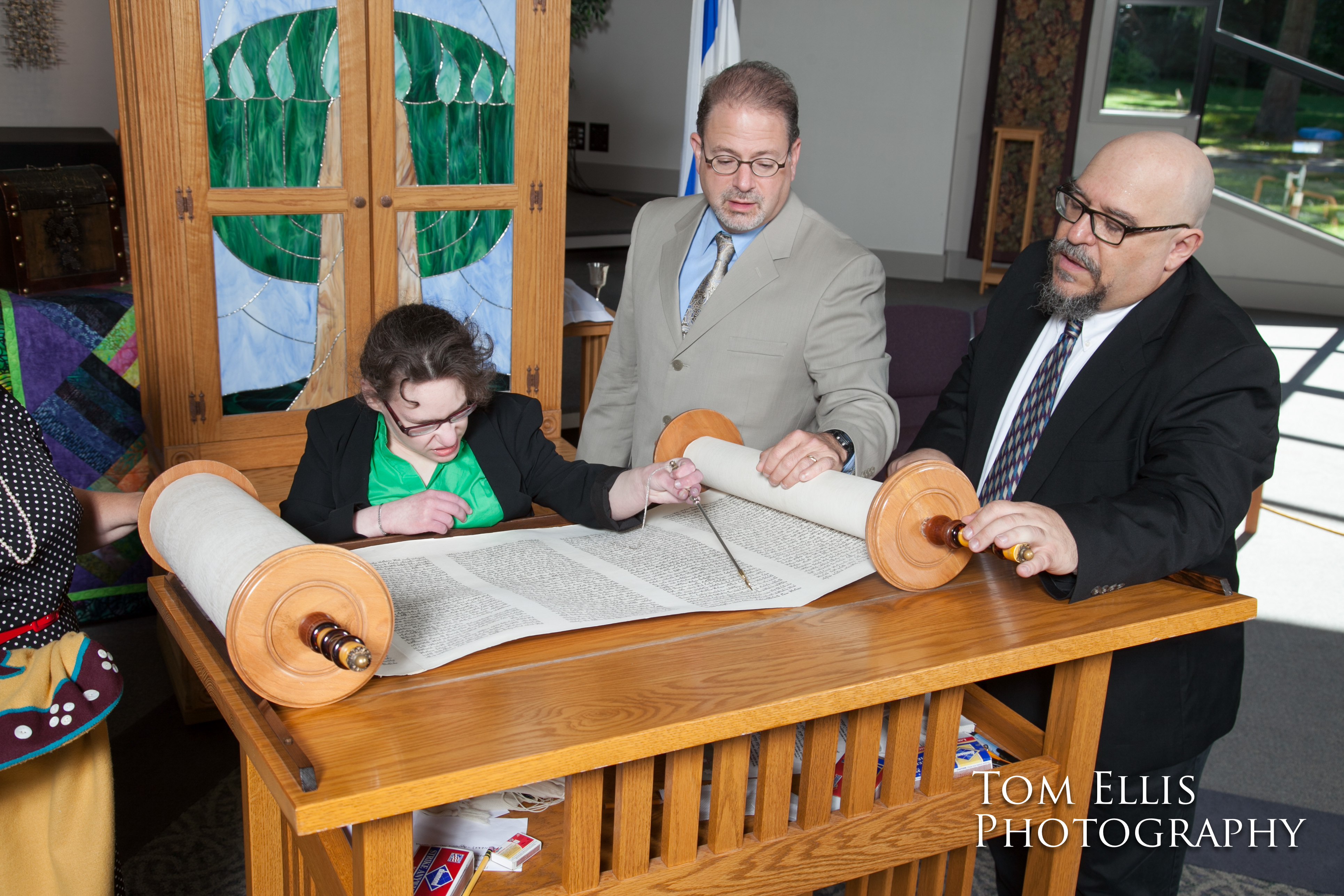 Becca reads the Torah at her Bat Mitzvah while her father and the Rabbi watch