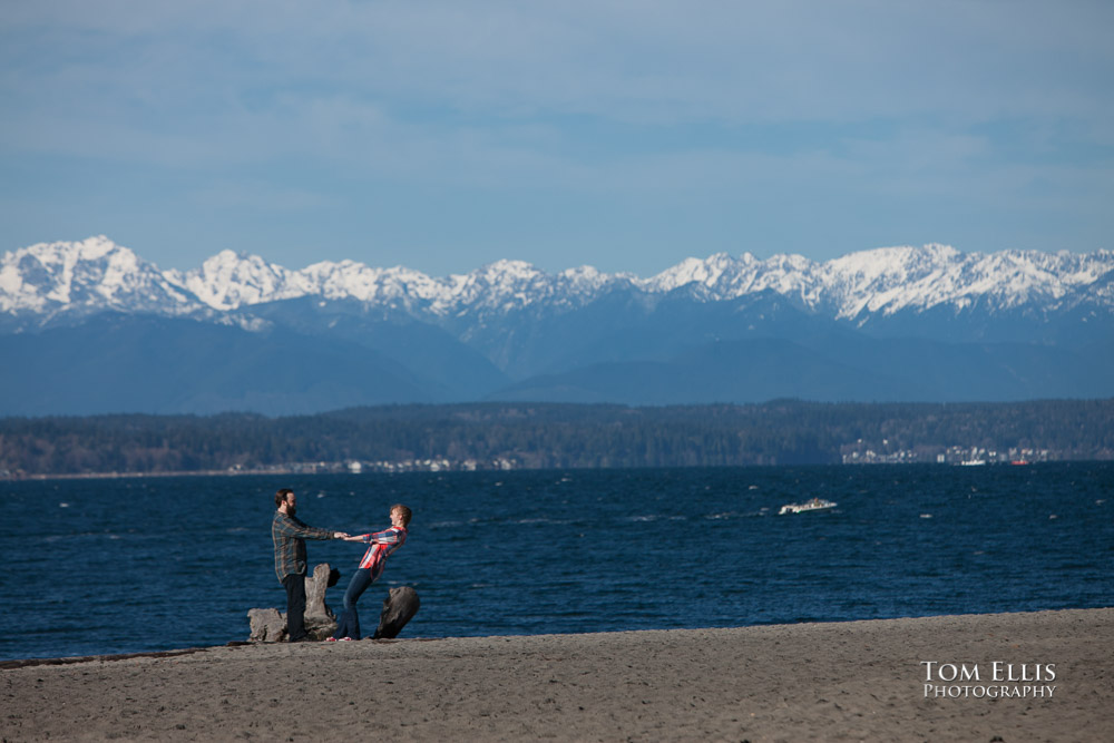 Couple dancing on beach during their engagement photo session, with the Olympic Mountains in the background