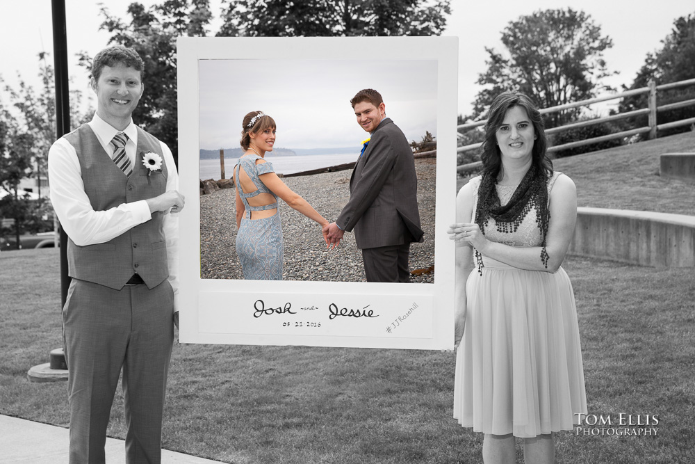 Black and white photo of Best Man and Maid of Honor holding picture frame containing a color photo of the bride and groom