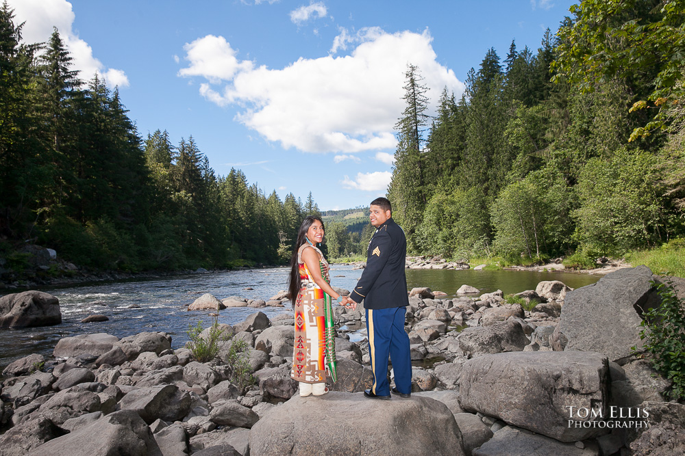 Man in dress military uniform with woman in Native American costume stand on large rock along the side of the Snoqualmie River