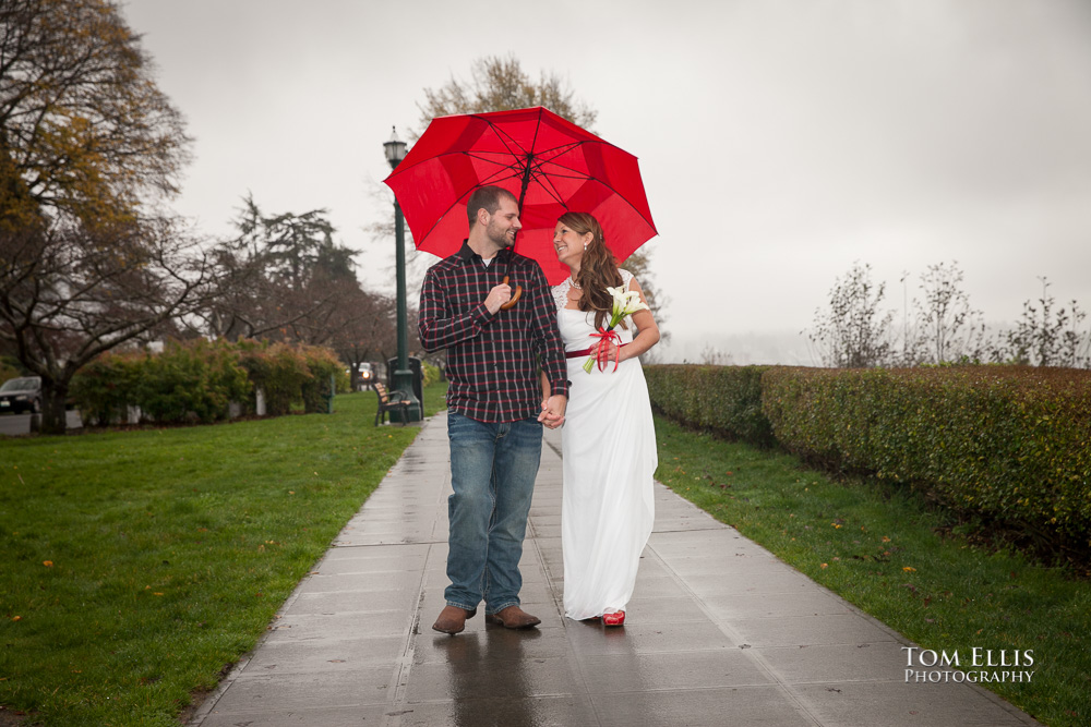 Couple walks under red umbrella before their Seattle area wedding ceremony in Grand Avenue Park