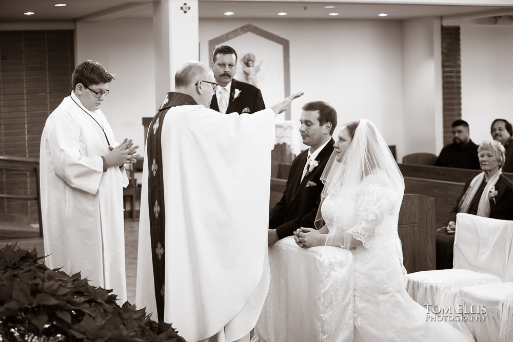 Sepia toned photo of wedding ceremony at Catholic church, as the priest blesses the kneeling couple just before pronouncing them married