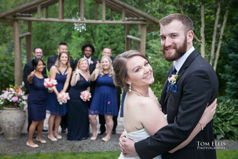 Bride and groom hug and smile for the camera, while the wedding party cheers in the background