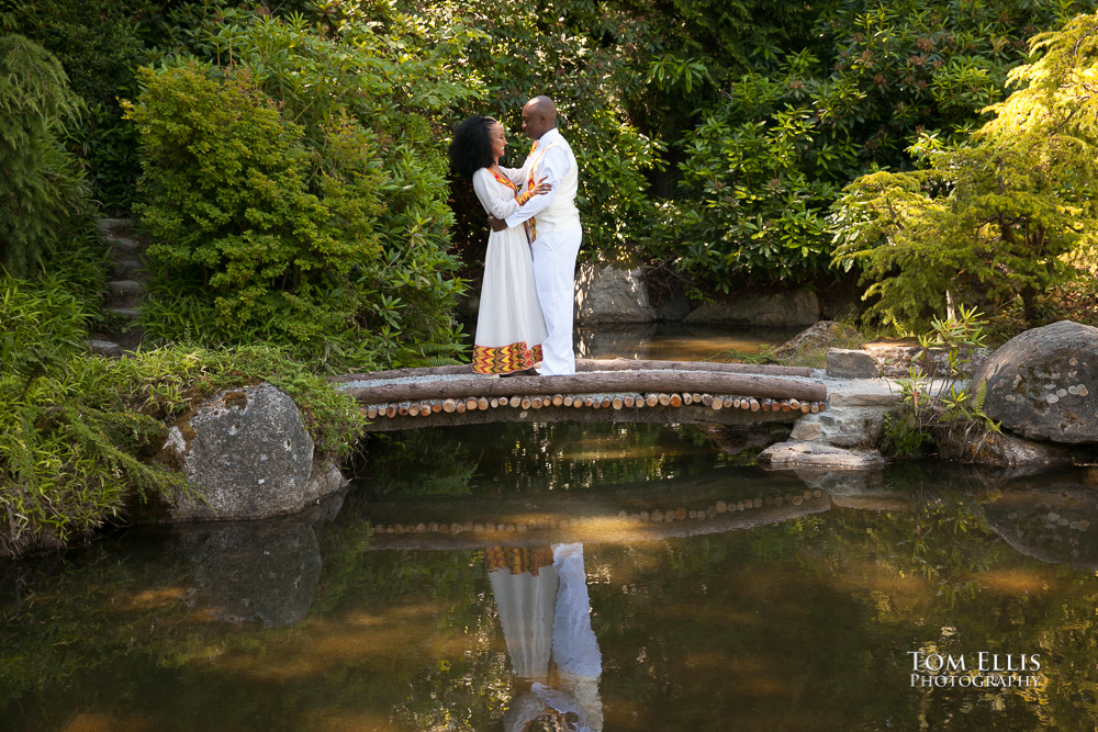 Couple dressed in traditional Ethiopian wedding costumes share a hug on one of the bridges at Seattle's Kubota Gardens during their wedding portrait session