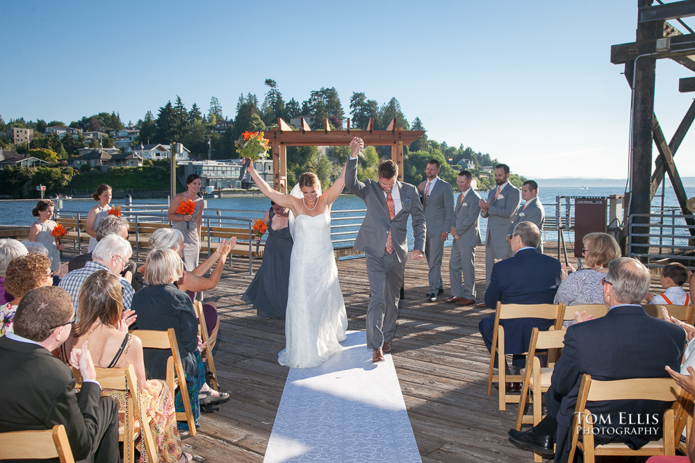 Bride and groom raise their hands over their heads in triumph as they recess down the aisle at the conclusion of their wedding ceremony at Ray's in Seattle