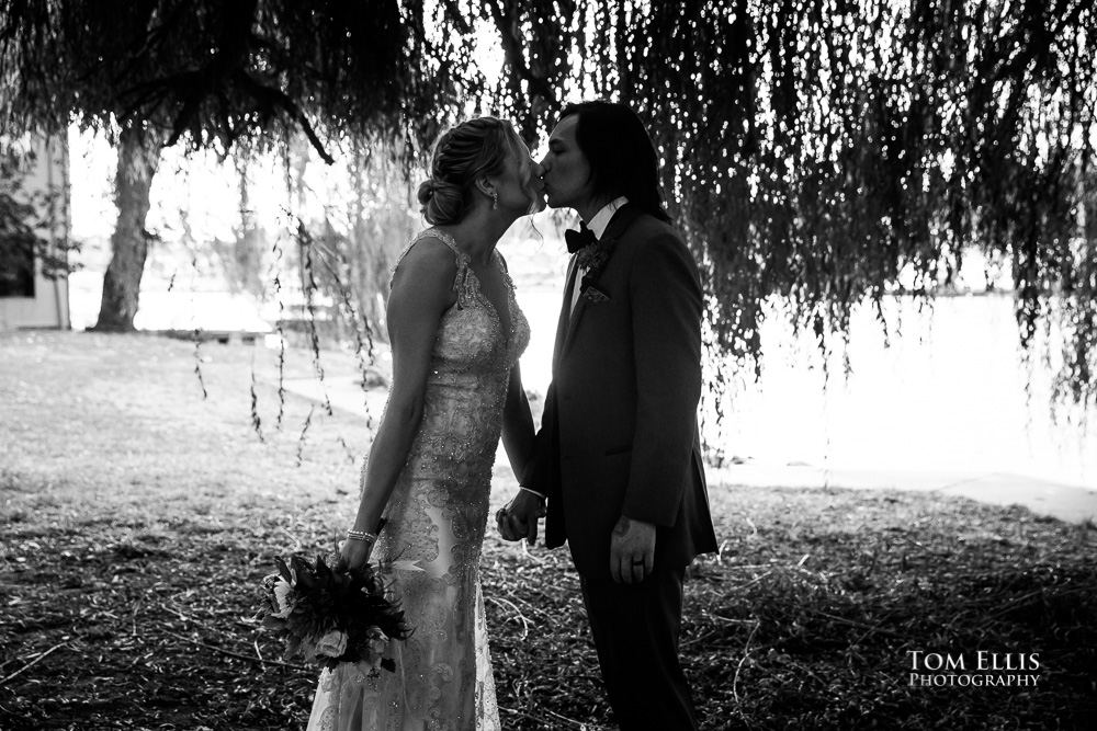 Black and white photo, silhouette of bride and groom kissing under a willow tree