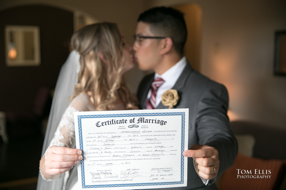 Bride and groom kiss while holding their marriage certificate up for the camera