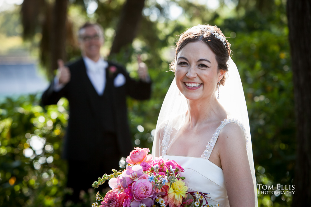 Bride stands in foreground while groom in the background gives a double "thumbs up" for the camera