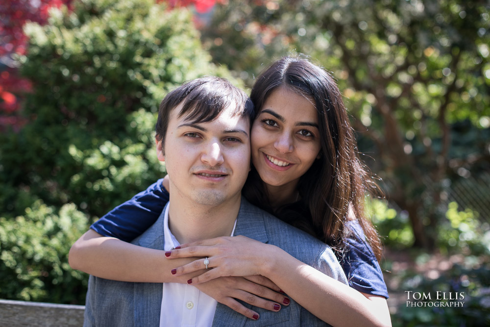 Beautiful young Indian woman hugs her fiance from behind while showing off her engagement ring during their Seattle engagement session at Kerry Park