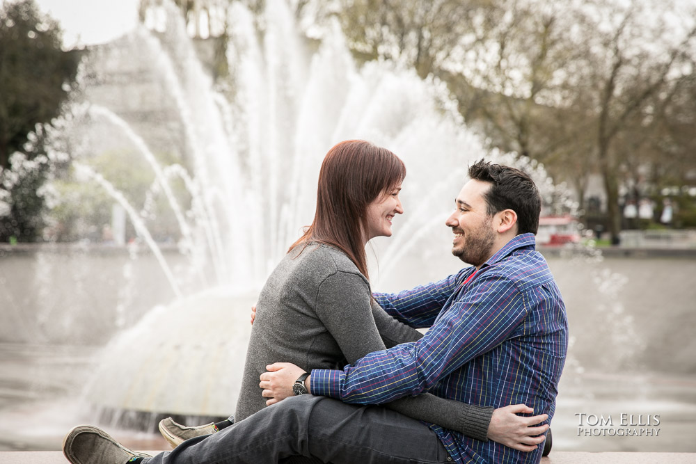 Engaged couple snuggle up close in front of the Center Fountain at the Seattle Center during their engagement photo session