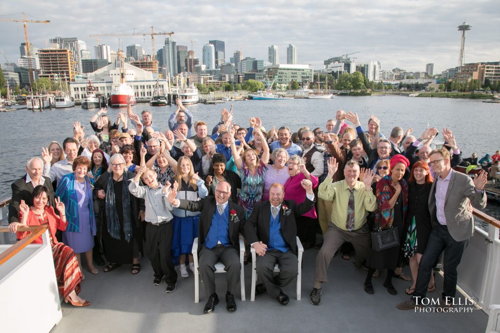 The two newlywed grooms and all of their family and friends gather together on the stern deck of the Emerald Star for a group photo during their wedding reception