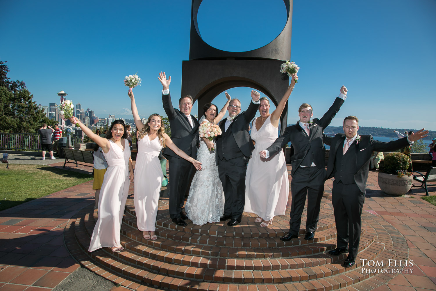 Norma, Jeff and their wedding party give a big "Hooray!" in front of the sculpture at Seattle's Kerry Park, before their Seattle wedding at Palisade