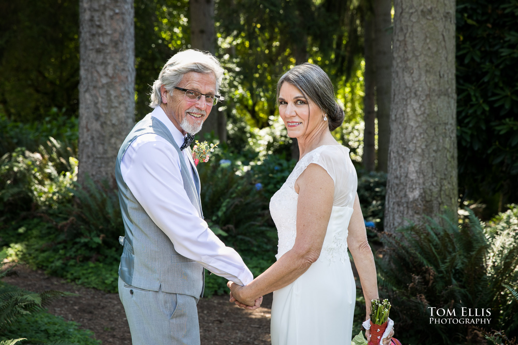 Bride and Groom turn and look over their shoulders while walking in the woods before their Seattle wedding at the DAR House