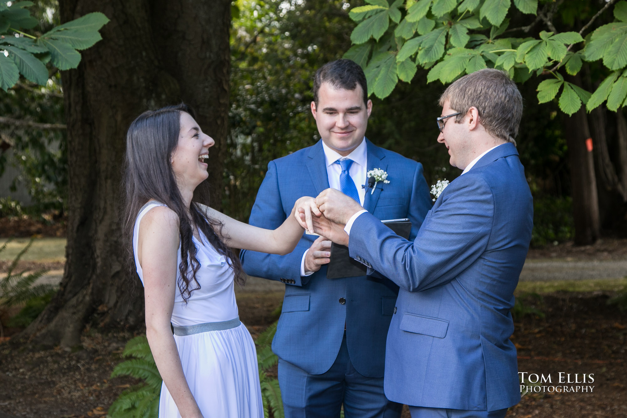 Bride breaks into laughter as the groom attempts to get the ring onto her uncooperative finger during their Seattle area wedding ceremony