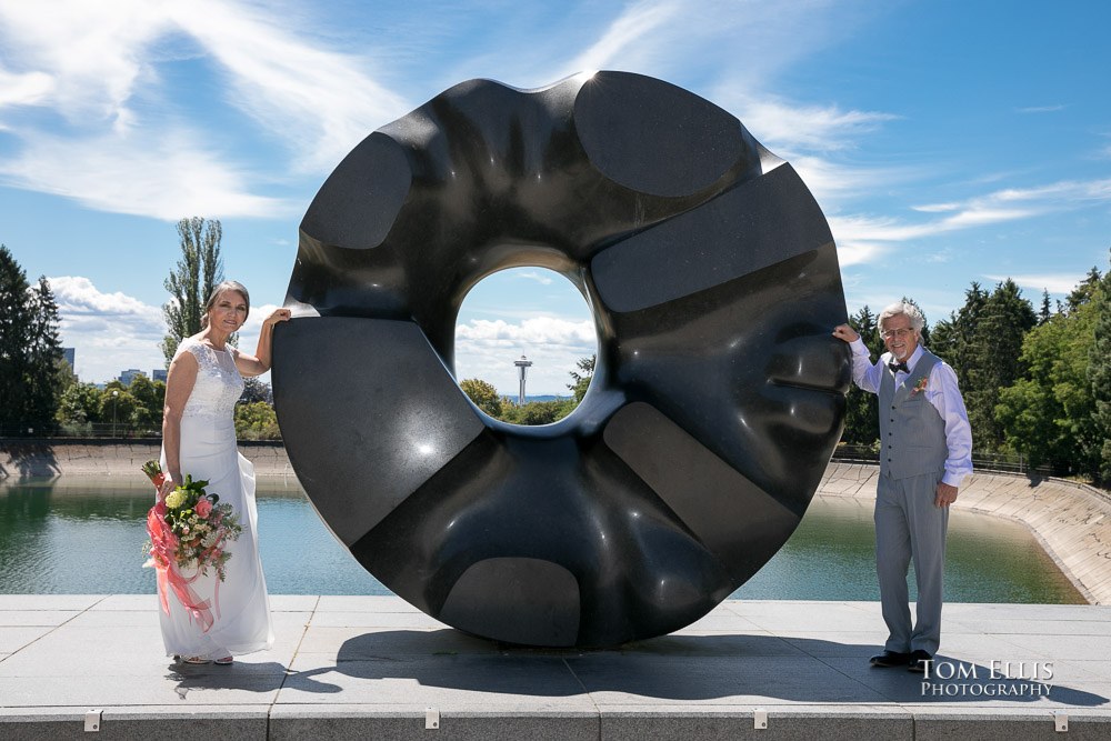 Bride and groom pose with the sculpture outside the Seattle Asian Art Museum at Volunteer Park, with downtown Seattle and the Space Needle in the background