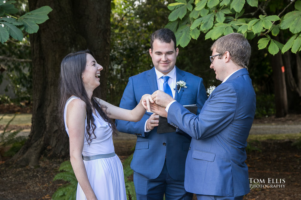 Bride Cassie laughs as groom Robert has some difficulty getting the wedding ring onto Cassie's finger during their Seattle outdoor wedding ceremony