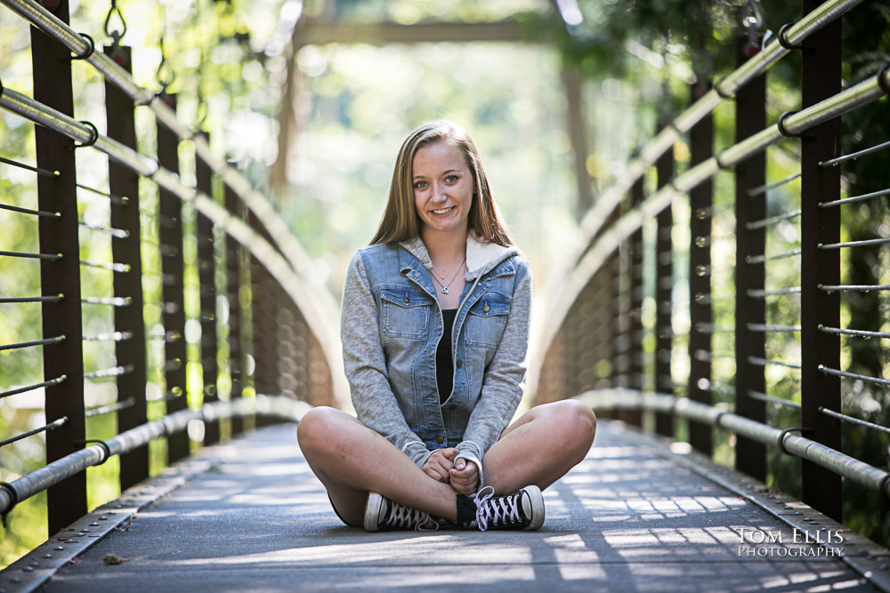 Pretty high school senior sitting cross-legged on a suspension bridge with beautiful backlighting