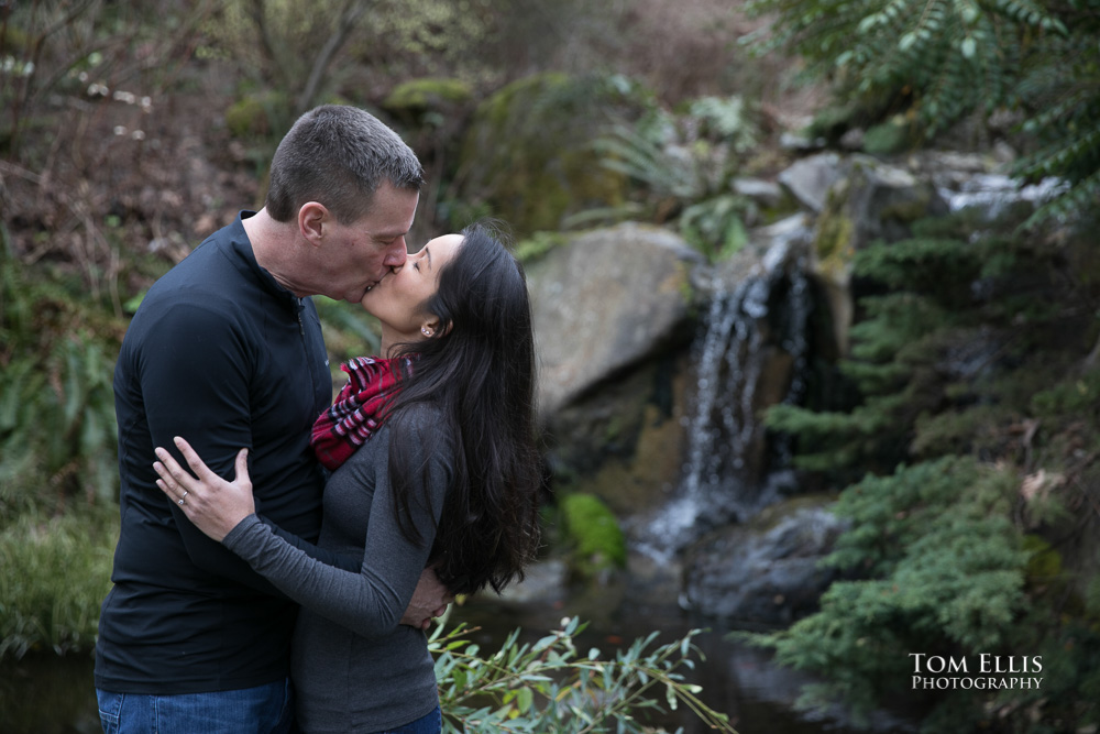 Elaina and Trip kiss near a waterfall during our Seattle area engagement photo session at the Bellevue Botanical Garden