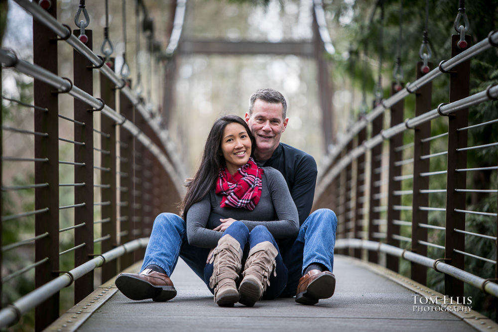 Elaina and Trip sit in the middle of the suspension bridge during our Seattle area engagement photo session at the Bellevue Botanical Garden