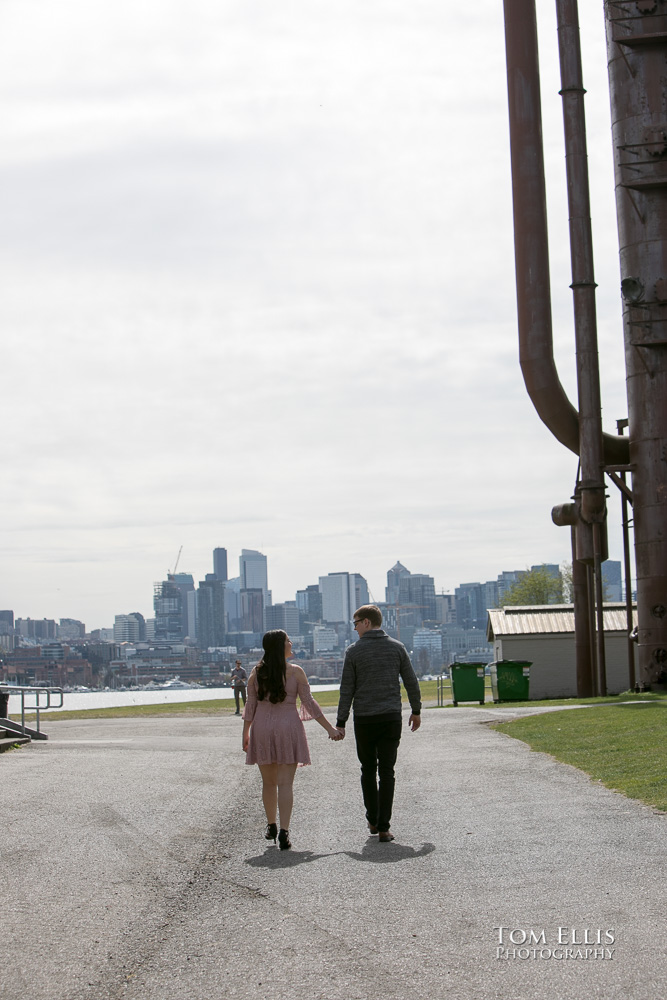Yoshimi and Jake walk together toward the Seattle skyline during their engagement photo session at Gas Works Park