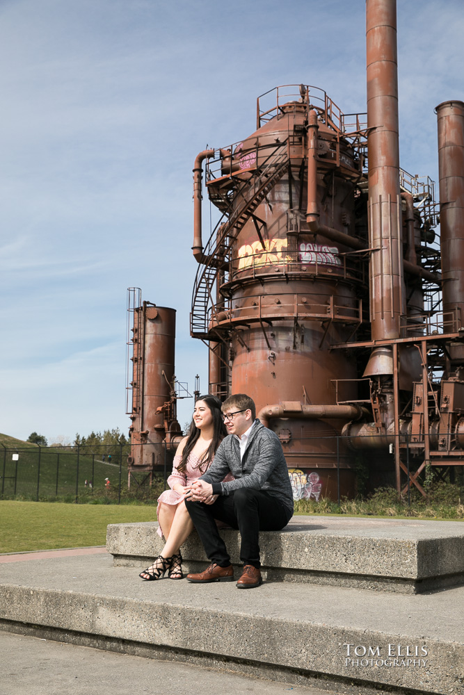 Yoshimi and Jake sit in front of the old gasworks during their engagement photo session at Gas Works Park