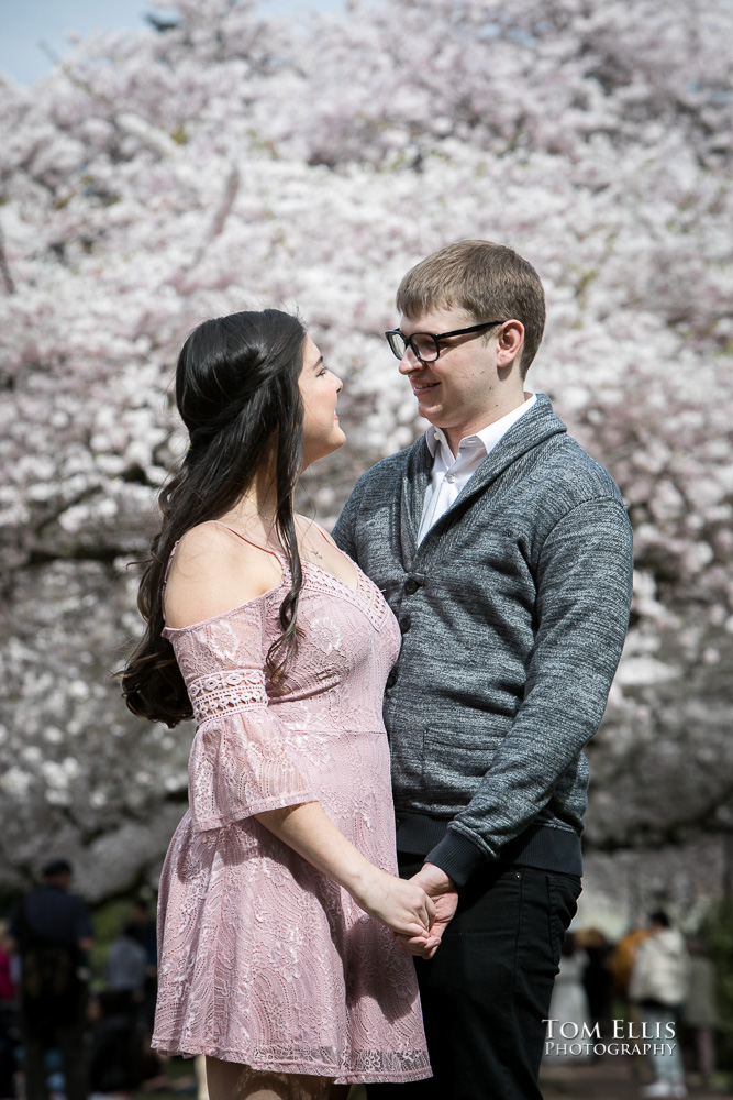 Yoshimi and Jake hug with the cherry trees in the background during their engagement photo session at the UW campus