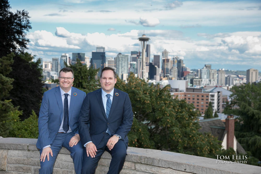 Newlywed same sex couple John and Terry sit on the wall at Kerry Park with the Space Needle and Seattle skyline in the background. Tom Ellis Photography, Seattle gay wedding photographer