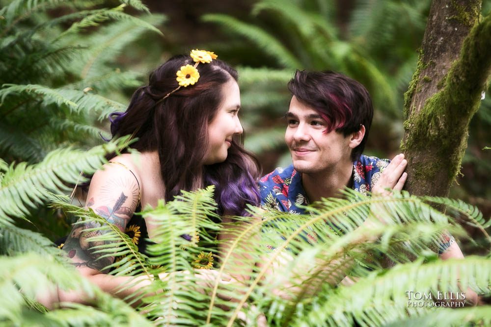 Aimee and Jordan crouch in the ferns during their Seattle engagement photo session at the Washington Arboretum