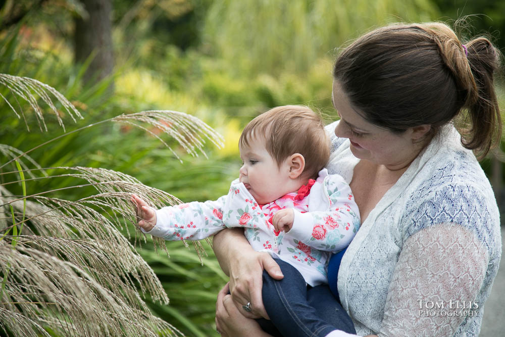 Mother holds her baby girl as she reaches out to touch some flowers in the Bellevue Botanical Garden. Tom Ellis Photography, Seattle family and baby photographer