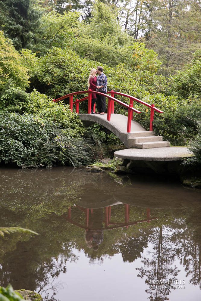 Kelly and David kiss while standing on top of the Moon Bridge in the Kubota Garden in Seattle during their engagement photo session. Tom Ellis Photography, Seattle engagement photographer