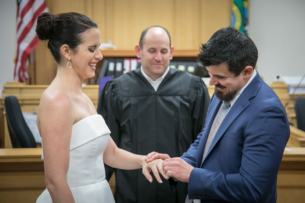 Austin tries to put the ring on Jocelyn's finger during their elopement wedding ceremony at the King County Courthouse in Seattle. Tom Ellis Photography, Seattle courthouse wedding photographer