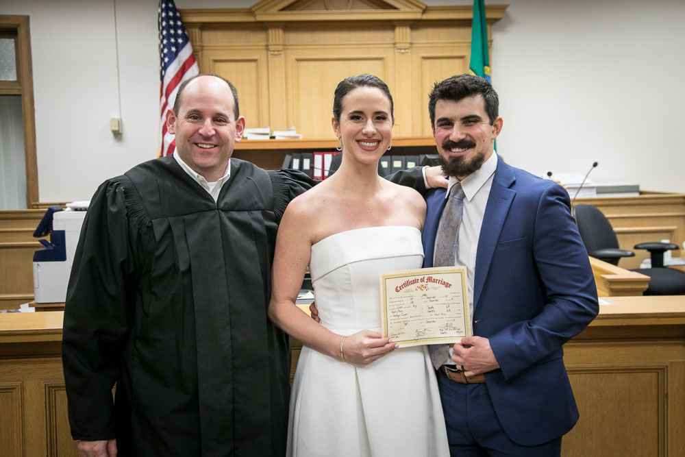 Judge Rosen, along with bride Jocelyn and groom Austin, display the marriage certificate for the newly married couple at the King County Courthouse. Tom Ellis Photography, Seattle courthouse wedding photographer