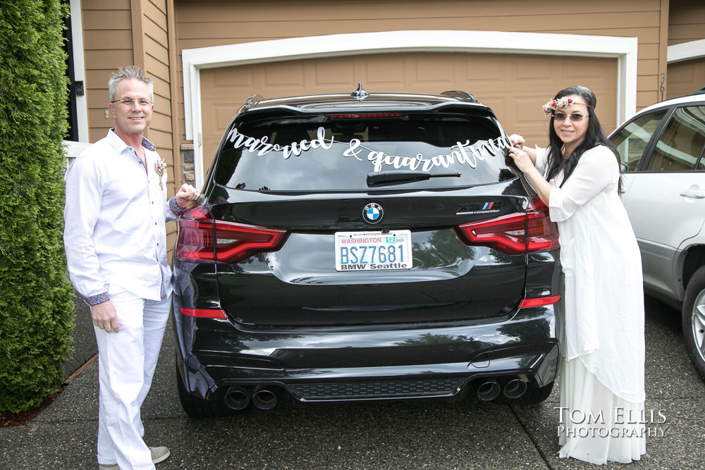 Bride and groom stand next to their car, decorated with a "Married and Quarantined" banner, after their elopement wedding. Tom Ellis Photography, Seattle elopement photographer